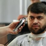 Barber guy gives a haircut to a bearded man sitting in a chair in a barbershop