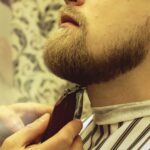 Barber shaves beard of client man on chair Barbershop. Beard Haircut.