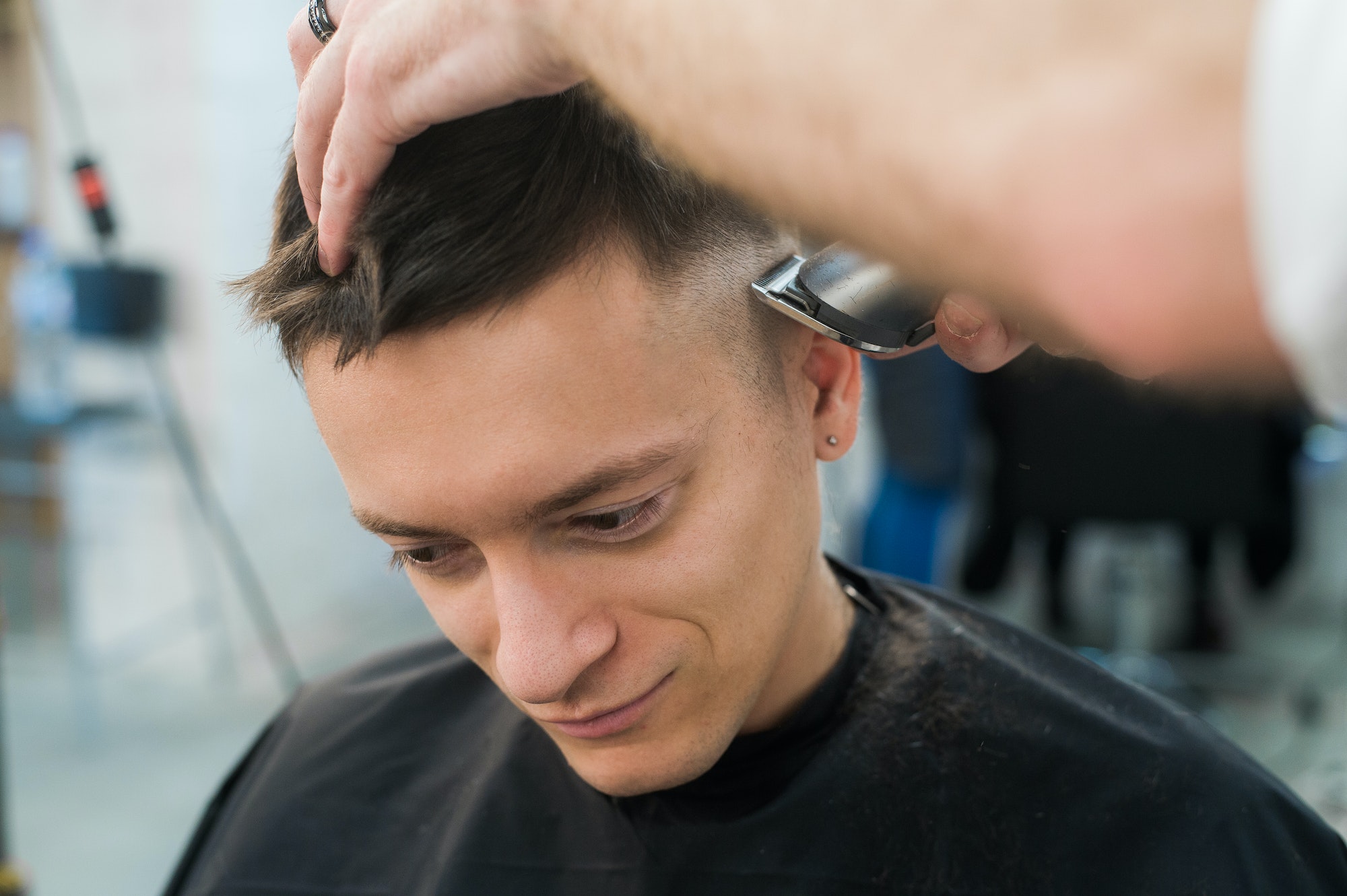 Professional styling. Close up side view of young man getting haircut by hairdresser with electric