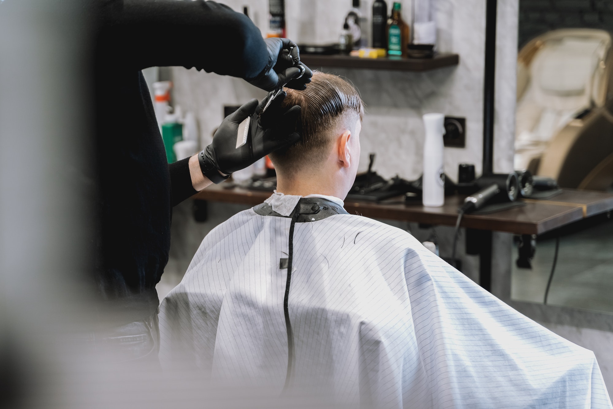 Visit to barbershop. Stylish man makes fashionable haircut. Barber, hairdresser, stylist with scisso