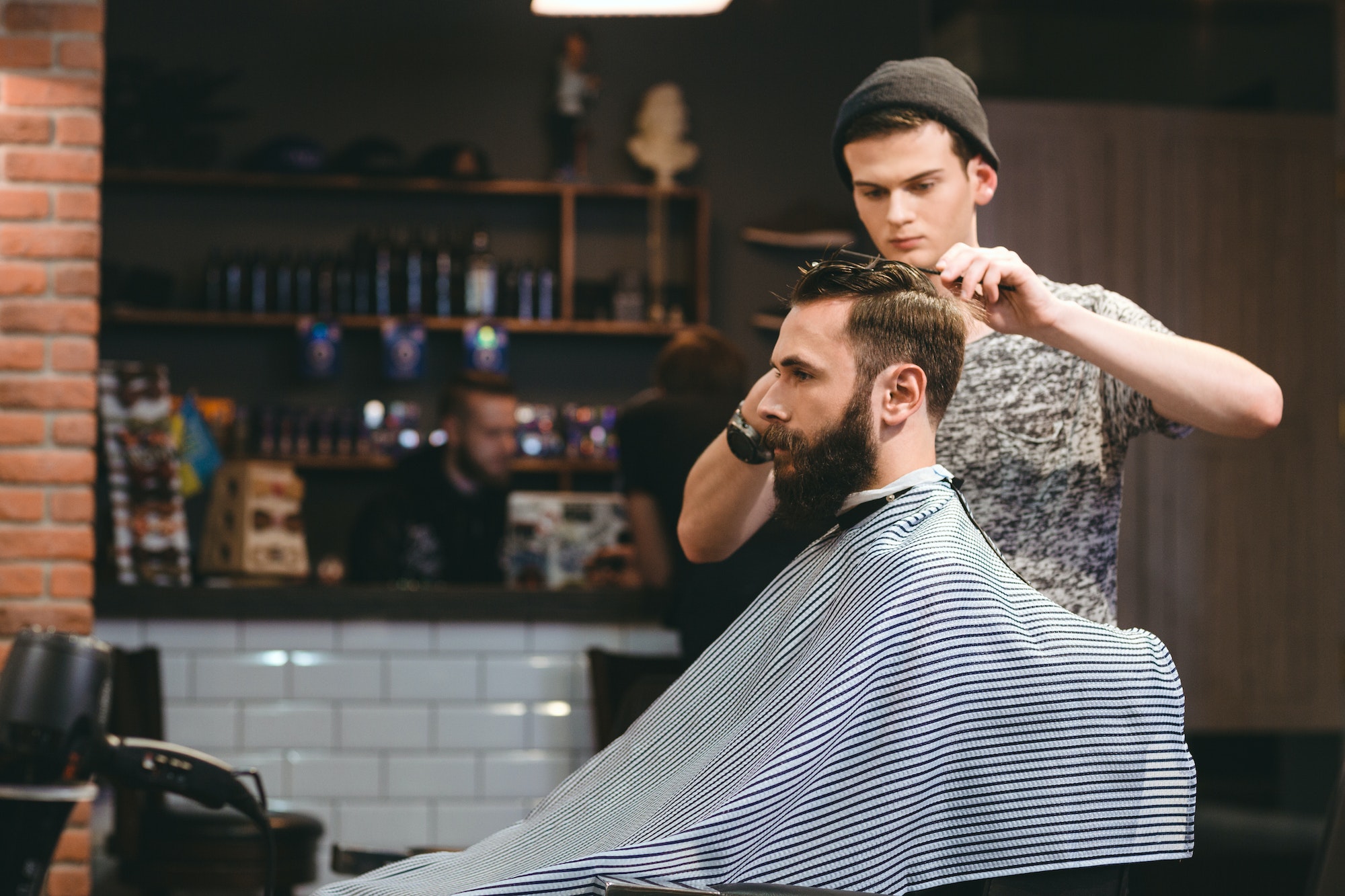 Young barber making haircut of bearded man in barbershop Young barber making haircut of bearded man in barbershop